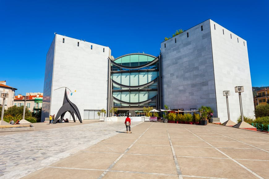 A solo figure stands looking towards a large modern building that houses Nice's Museum of Modern and Contemporary Art