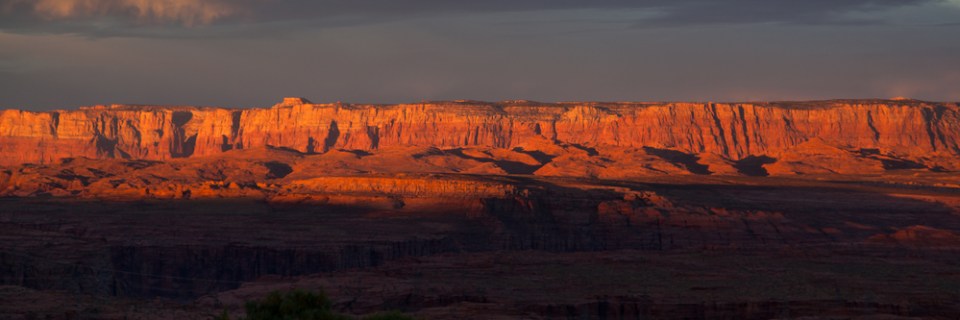 The Vermillion Cliffs National Monument lit by the early morning sunrise creating a fiery glow with dark storm clouds in the distance.