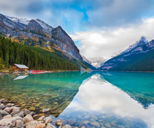 Clear turquoise lake, with a cottage and mountains in the background