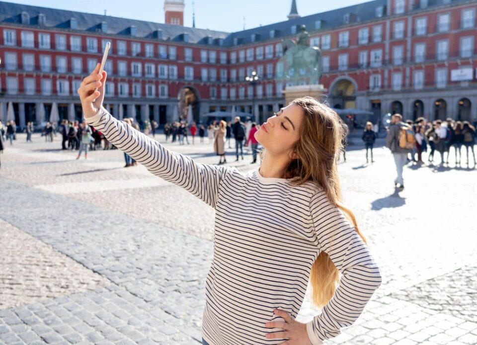 Beautiful young caucasian student tourist woman taking a selfie or video for her tourism and travel around the world blog web in Plaza Mayor Madrid Spain. In social media and vacations in europe.