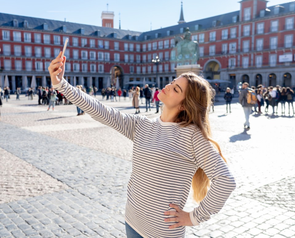 Beautiful young caucasian student tourist woman taking a selfie or video for her tourism and travel around the world blog web in Plaza Mayor Madrid Spain. In social media and vacations in europe.