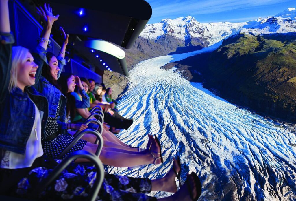 People riding the FlyOver Iceland ride and enjoying the view of a glacier on screen.