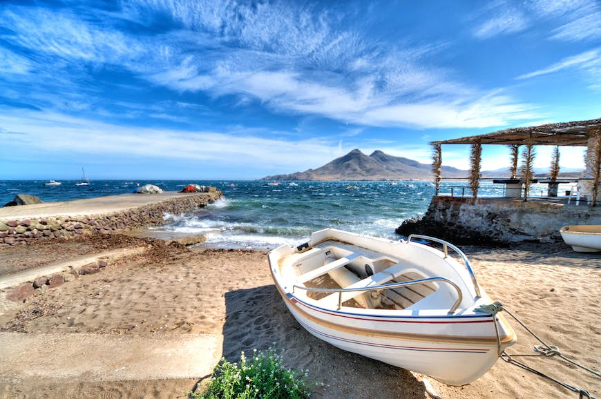 A small empty boat on the sandy shore, with an island out at sea