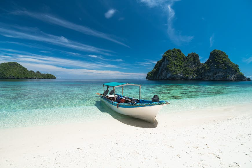 A small dive boat anchored on a bright white sandy beach