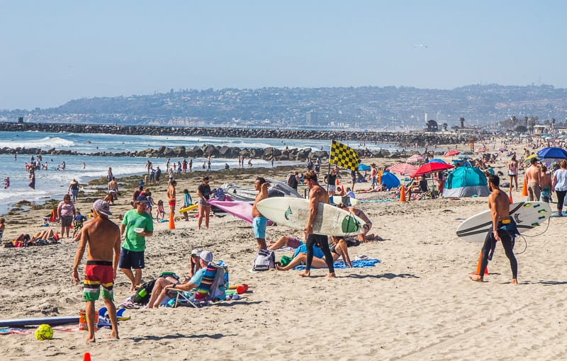 surfers holding baords on the sand and many peopl on Ocean Beach