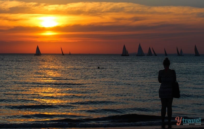 woman looking at Sunset on St Kilda Beach with silhouette sailboats