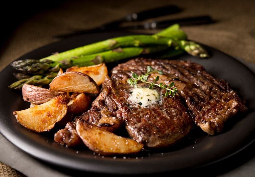 Cognac-marinated grilled ribeye steak with steak fries and asparagus on a ceramic plate.