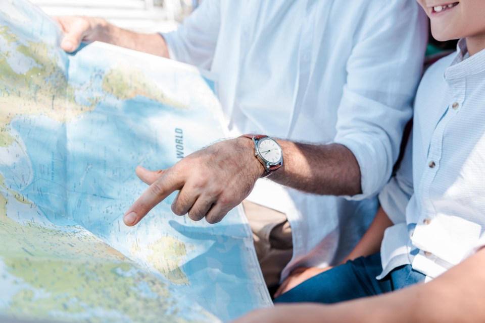 cropped view of father pointing with finger at map near happy son