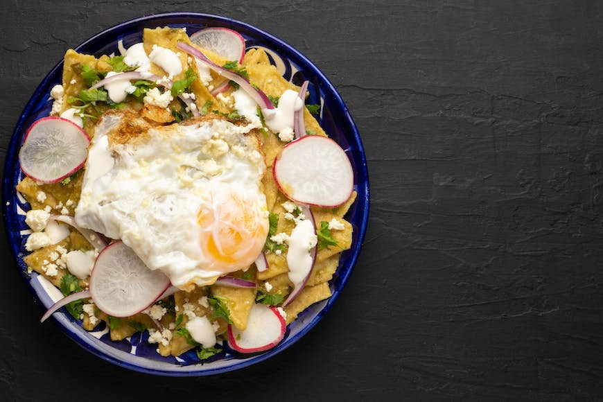 A plate of Mexican green chilaquiles with fried egg and cheese on a table