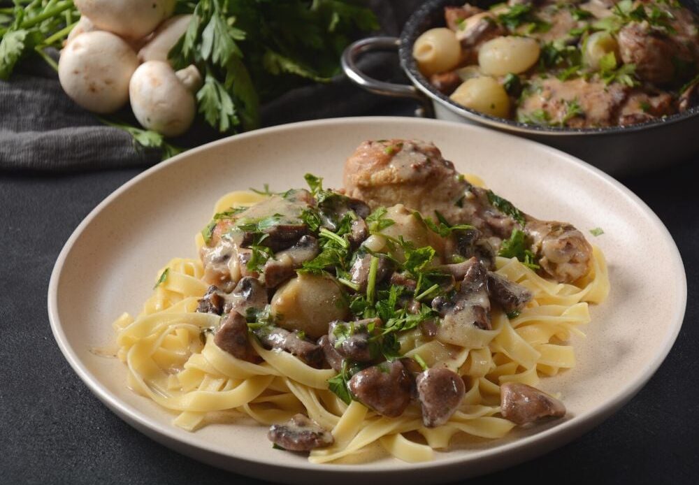 Fricassee is chicken stewed in a creamy sauce with mushrooms on a white plate on a black tablecloth.