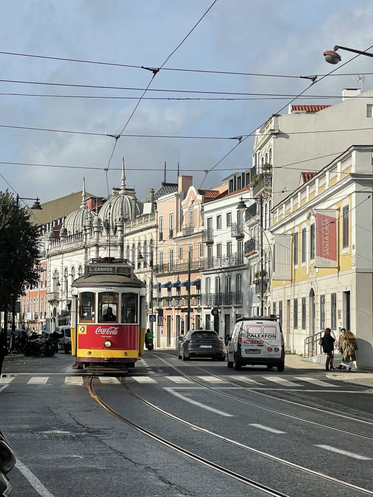 A red and yellow streetcar coming down a street in Lisbon.