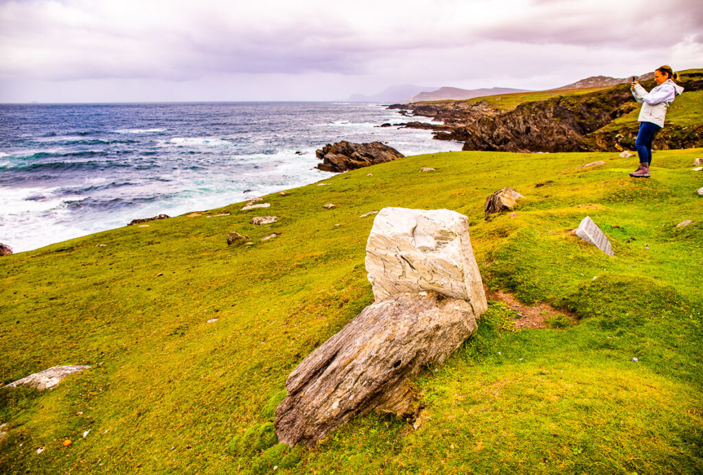 A large rock and lady on a cliff edge overlooking the ocean