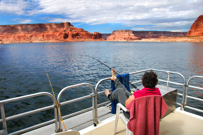 Woman relaxes and enjoys the fantastic views of sandstone cliffs and blue skies.  She is on a houseboat on Lake Powell in Arizona.  She fishes holding the rod with her toes.
