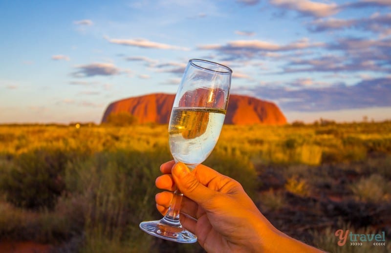 a hand holding a glass of wine in front of uluru