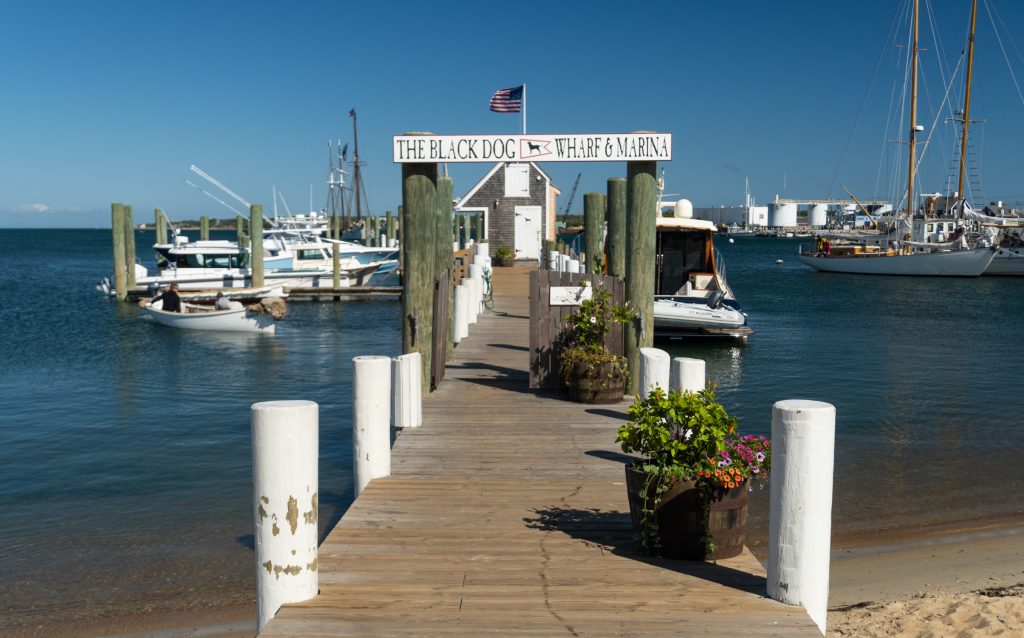 A wooden dock leading out to calm blue water and lots of small fishing boats.