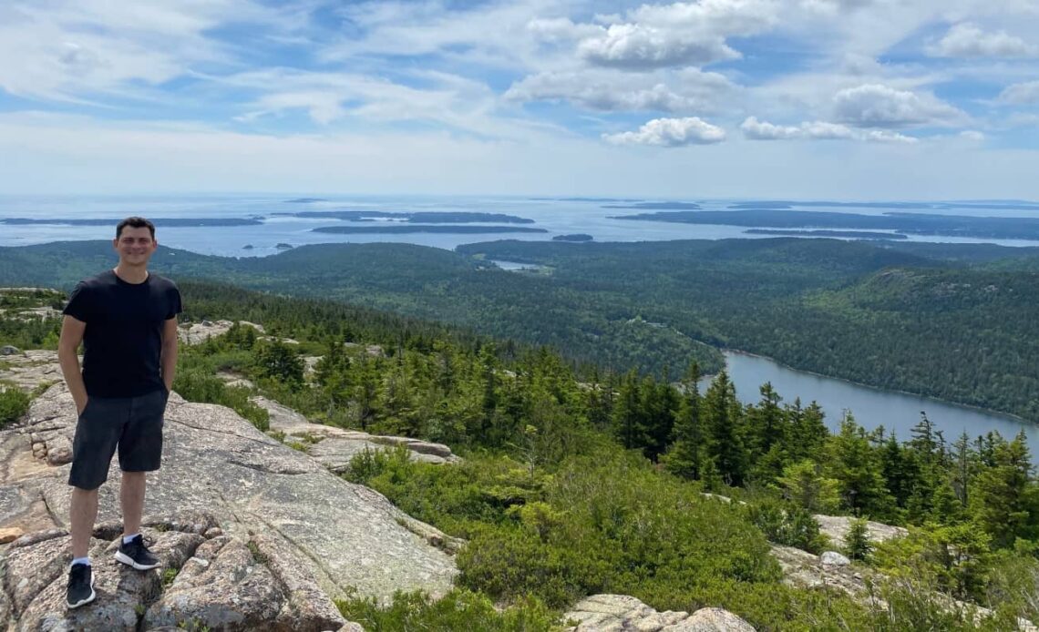 Matt standing on top of a mountain with a lush archipelago behind him in Maine, USA