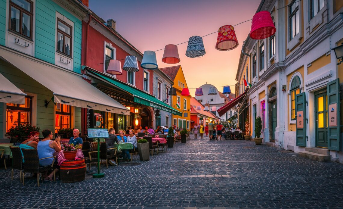 People seated at restaurants and coffee shops in the old town of Szentendre during sunset.