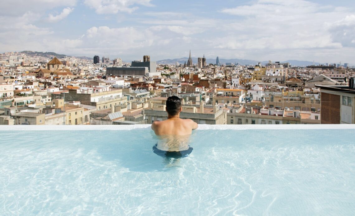Rear view of a young man relaxing in the pool and looking at Barcelona city skyline