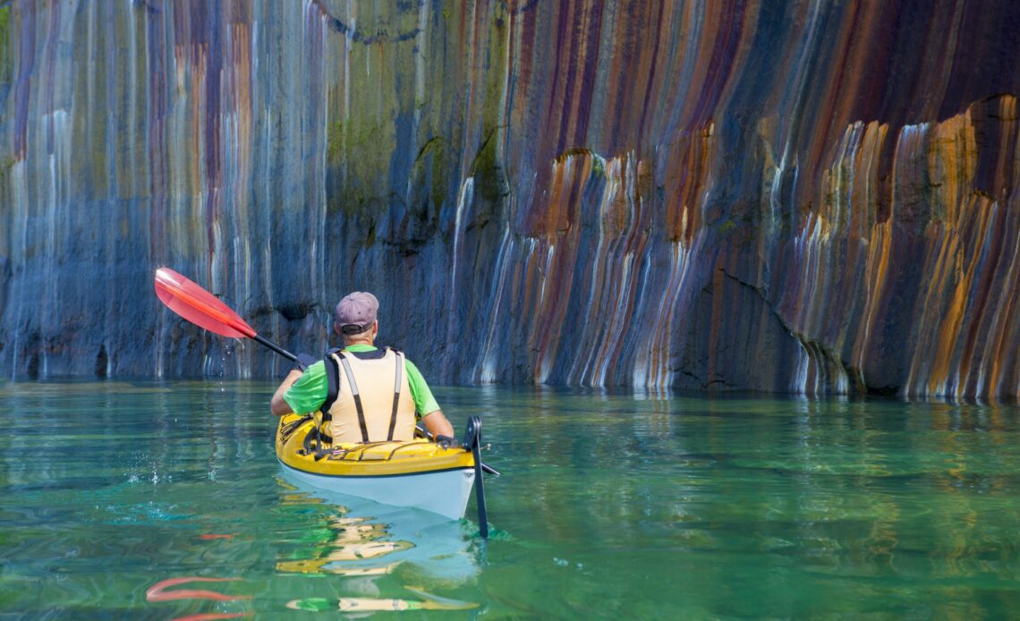 A man in a kayak approaches the multi-colored cliffs at Pictured Rocks National Lakeshore, Lake Superior, Upper Peninsula, Michigan, USA