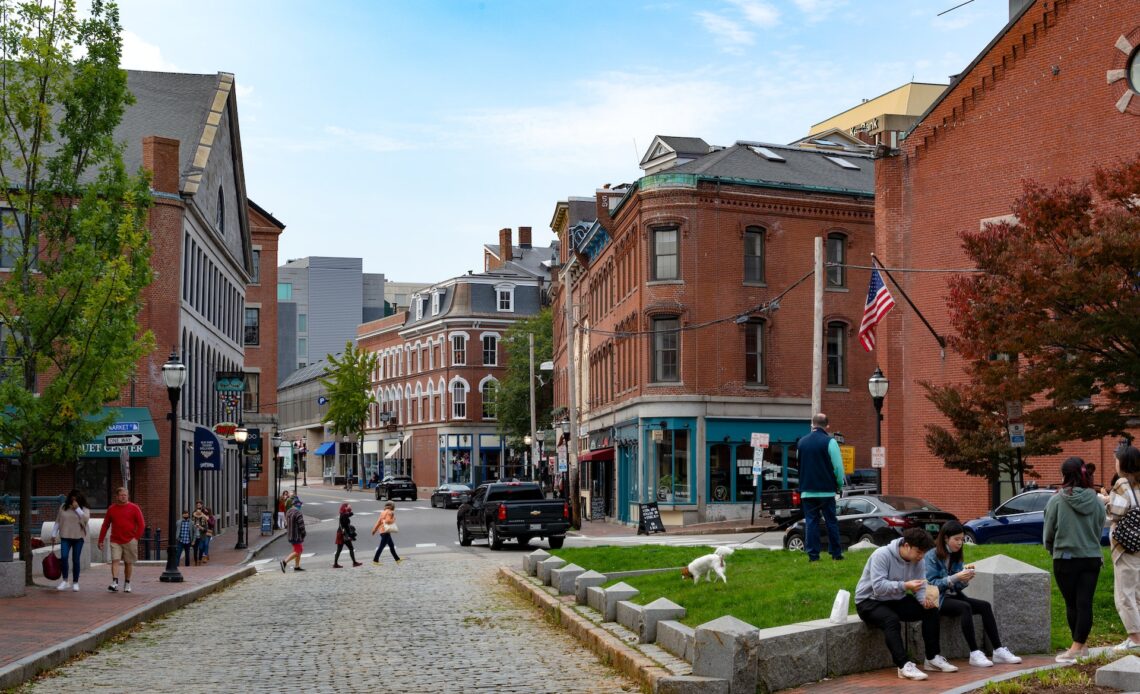 People walking around and hanging out in the Historic Waterfront District of Portland, Maine, with cobblestone streets and red-brick buildings.