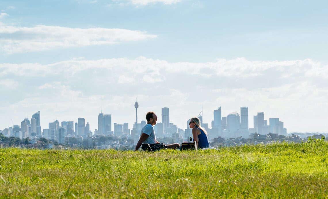 Couple Sitting On Field with Sydney skyline in the background