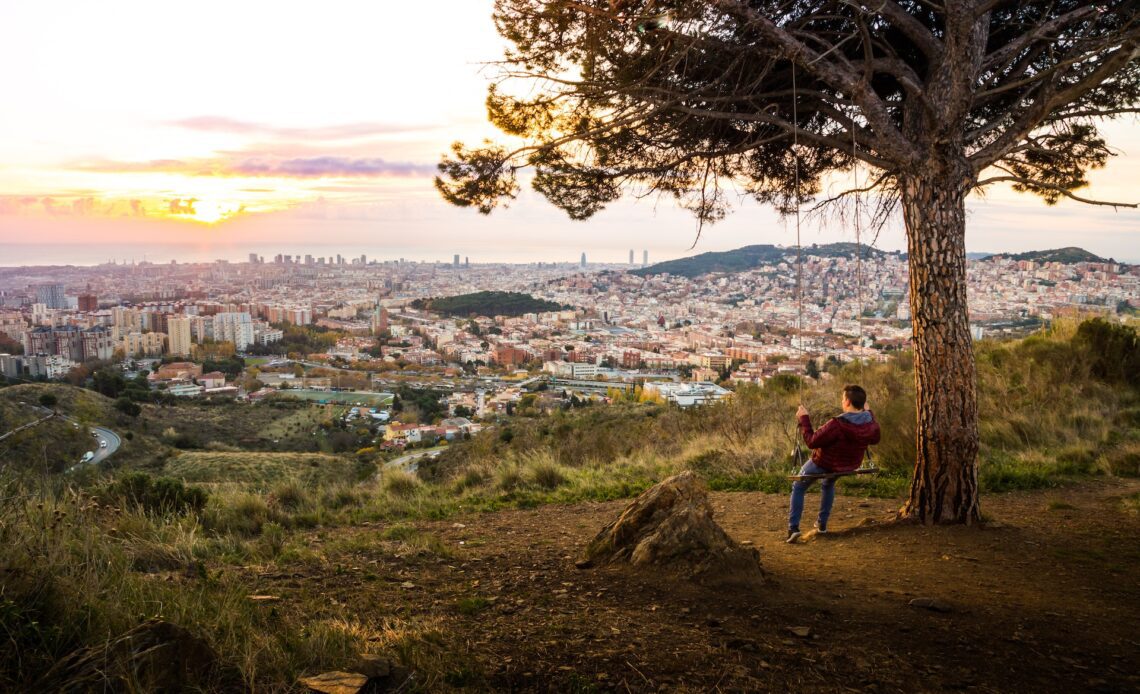 Guy enjoying sunrise over Barcelona city from the tree swing in Collserola