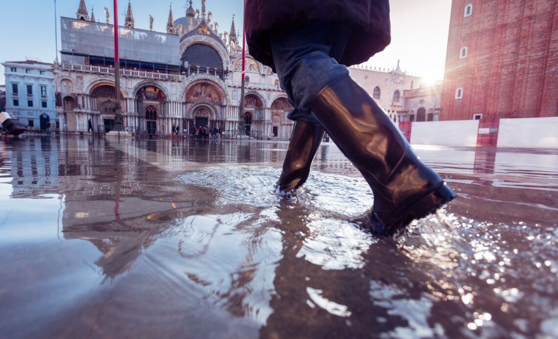 A woman in rubber boots walking over St Mark's square in Venice during acqua alta in venice