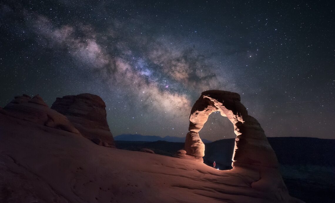 A person stands under Delicate Arch watching the Milky Way, Arches National Park, Moab, Utah, USA