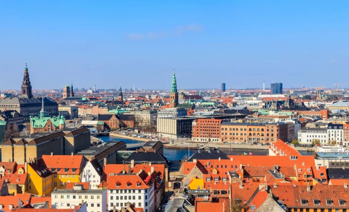 Aerial view of Copenhagen, Denmark, with red rooftops, a canal, and church steeples dotting the cityscape