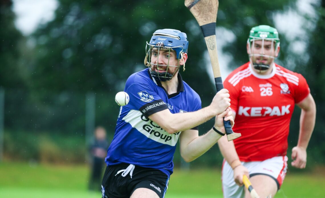 A helmeted hurling player in blue grimaces as he prepares to whack the sliotar