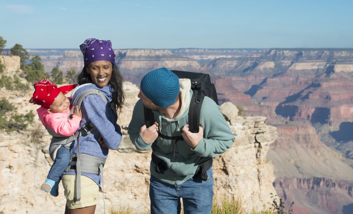 Young mixed-race family hiking at the Grand Canyon, the mother carrying their baby in a carrier on her back and the father playing with her.
