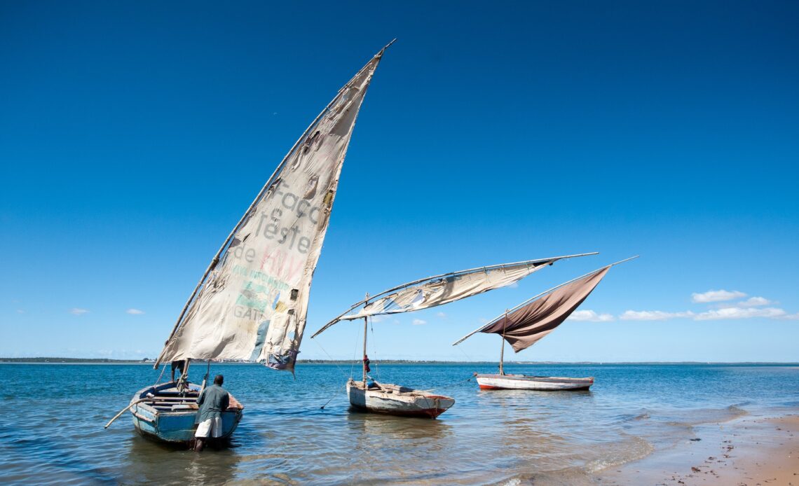 Three small masted boats unfurl their sales on the shores of Lake Malawi
