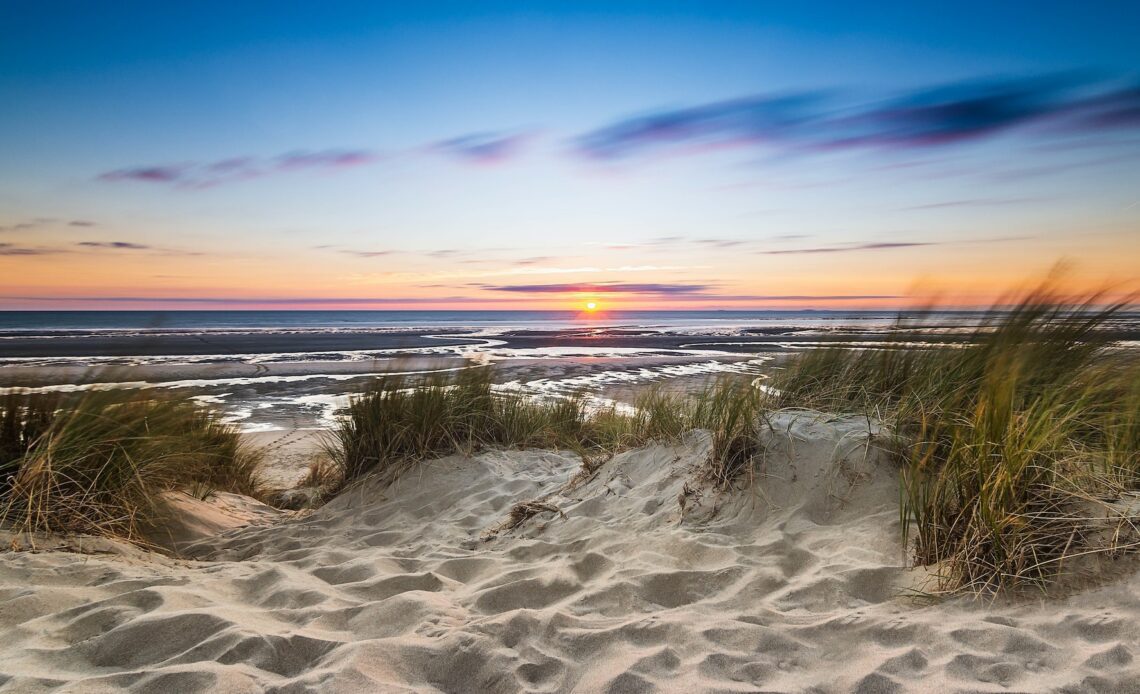 Sand dunes on the edge of a body of water with the sun setting