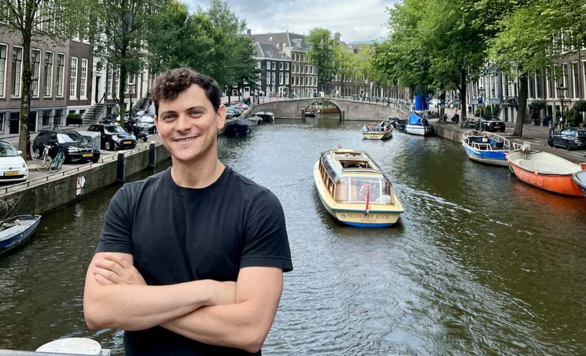 Nomadic Matt posing by a narrow canal in sunny Amsterdam