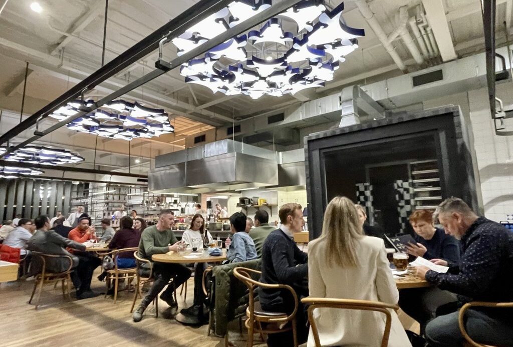 People eating in a restaurant with chandeliers made of lights in the shape of cows' heads.