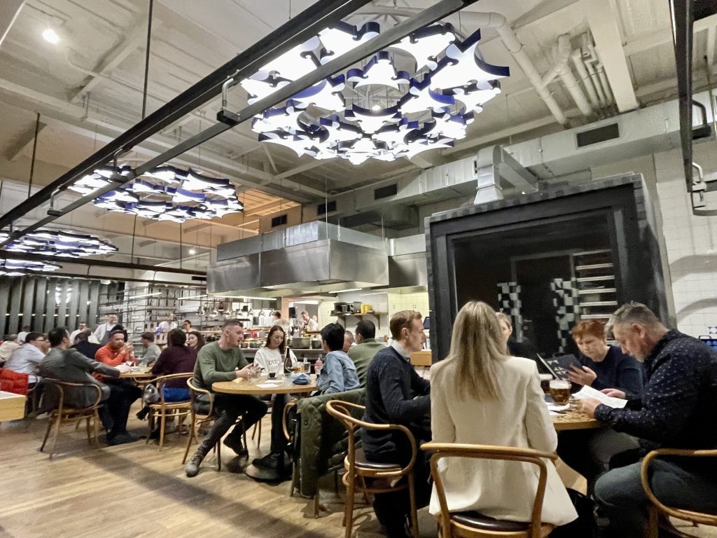 People eating in a restaurant with chandeliers made of lights in the shape of cows' heads.