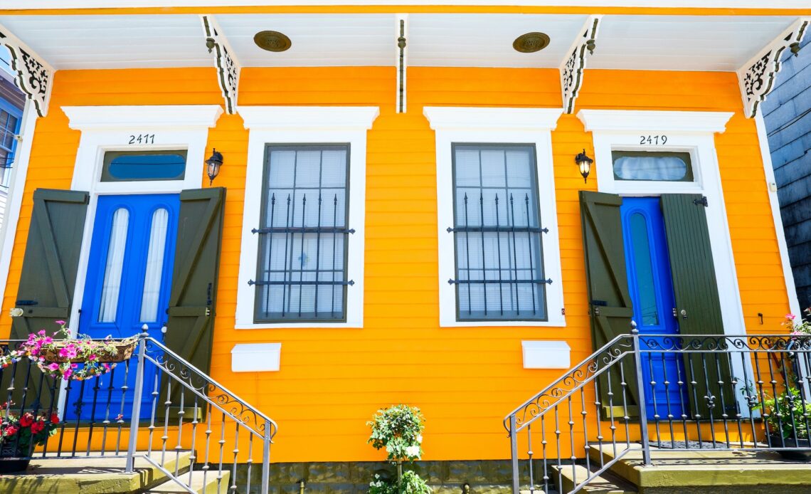 The front of a colorful historic house painted yellow with blue doors