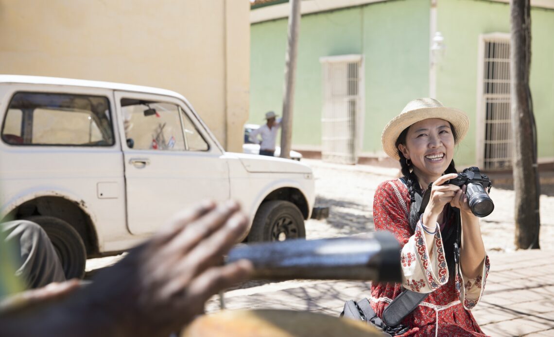 A woman holding a camera smiles and sat near her car at someone