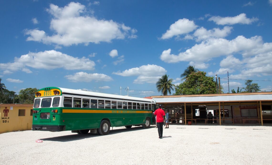 A 1950s-style green school bus is parked at a bus station in Belize City