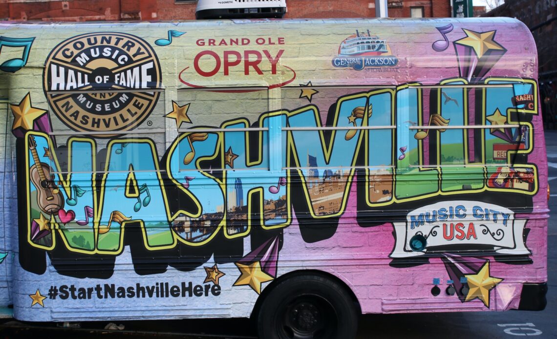 The side view of a parked bus which is emblazoned with 'Nashville' on the size parked in the city of the same name