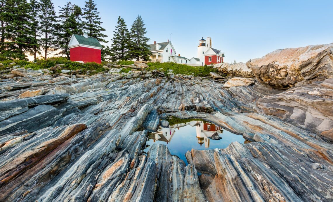 The characteristic "gneiss" rocks along the coast of the Pemaquid Peninsula allows for water to form in recesses. The lighthouse is reflected on this water surface. The Pemaquid Point Light is a historic U.S. lighthouse located in Bristol, Lincoln County, Maine, at the tip of the Pemaquid Neck