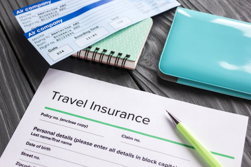 Travel insurance application form with flight tickets and passport on gray wooden desk