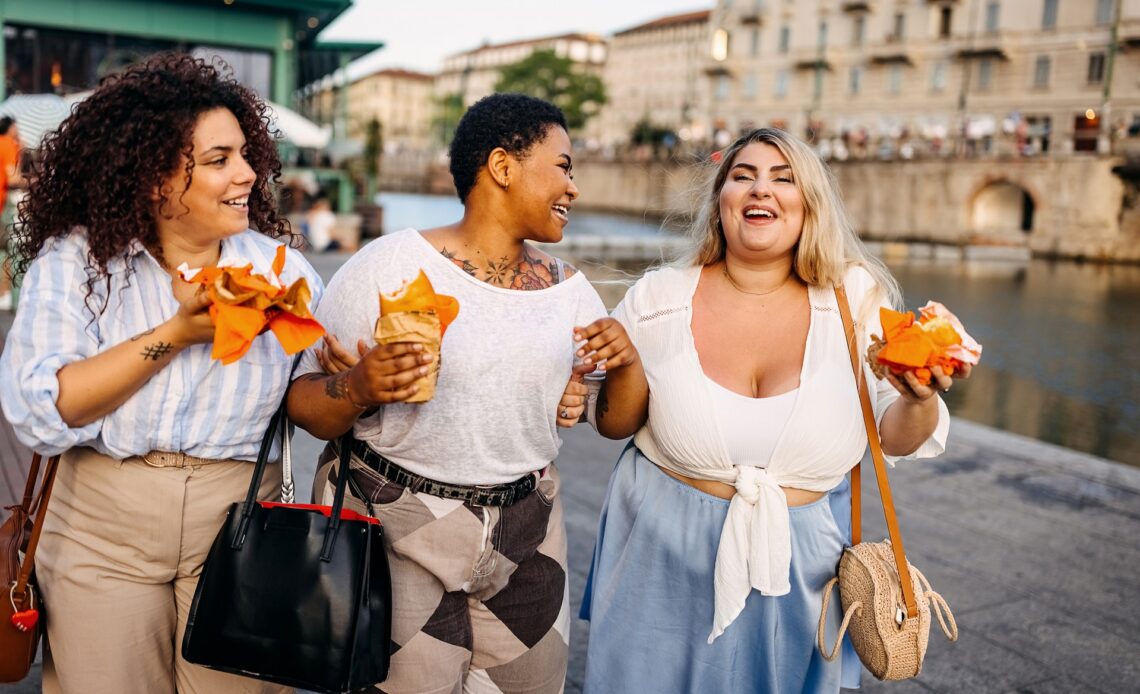 Three women eating fast food as they walk along a street in Italy