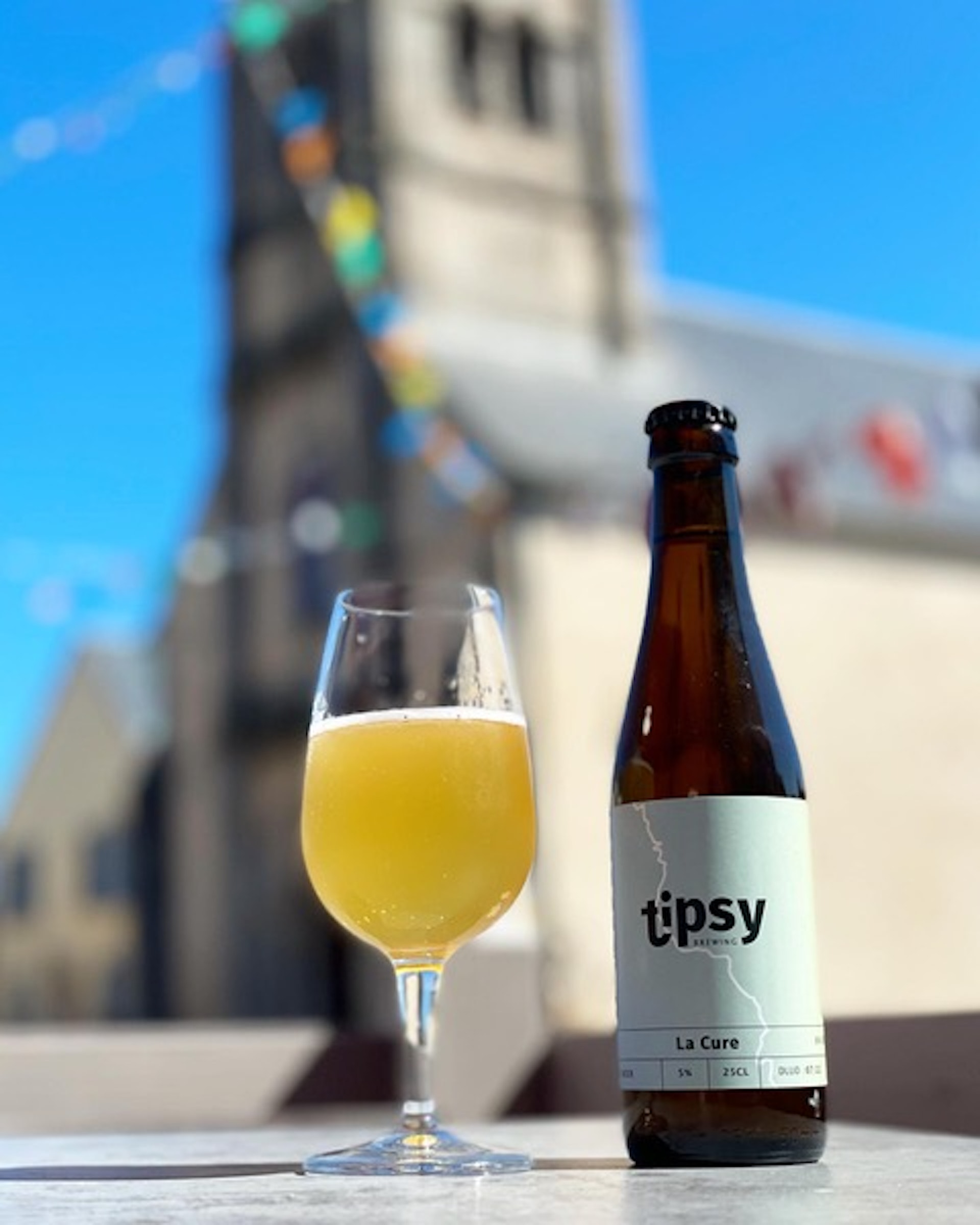 A beer and bottle sit on top of a barrel in front of a church. 