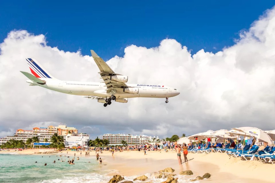 A commercial airplane approaches Princess Juliana airport above onlooking spectators on Maho beach.
