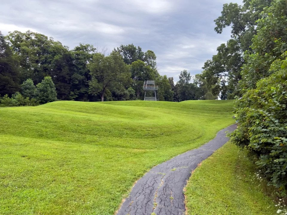 Walking path leads past curving body of a prehistoric Native American snake earthwork effigy mound at Great Serpent Mound in Ohio. 