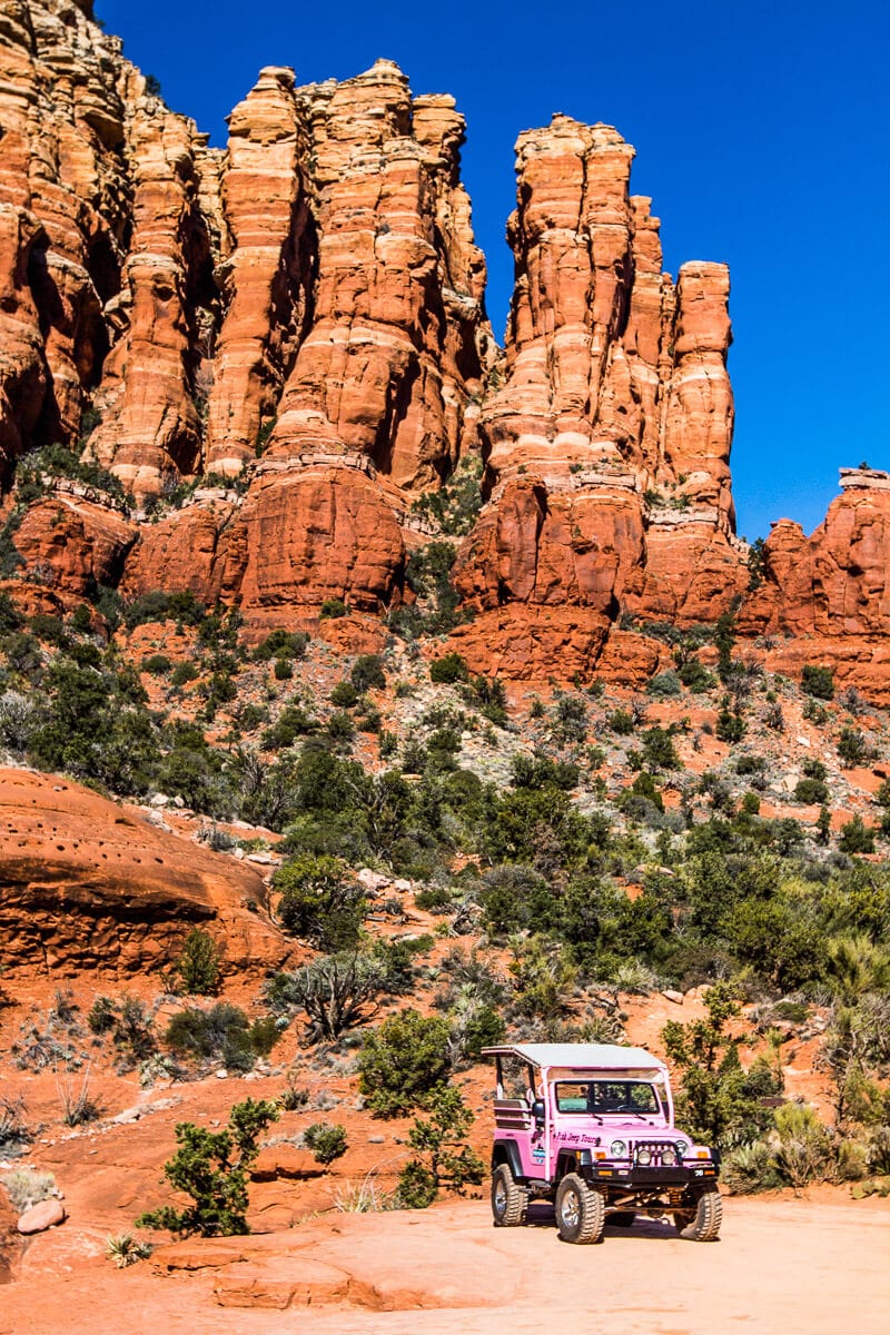 pink jeep beside looming red cliffs of Sedona