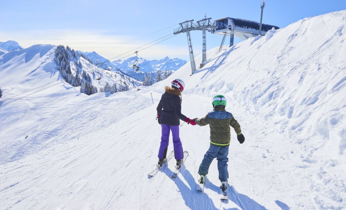 Two young children in full ski gear navigate their way towards a slope