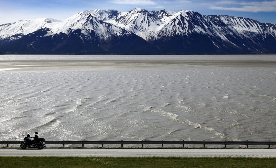 A person on a motorcycle drives by the water of Turnagain Arm on a road trip in Alaska