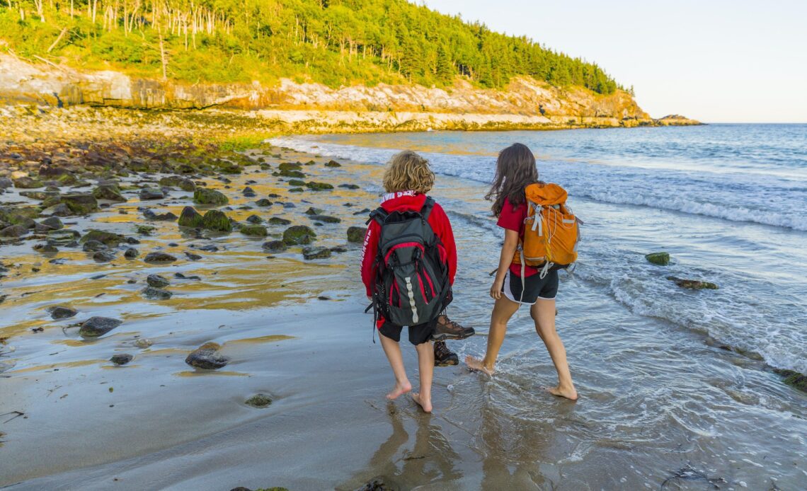 A teenage boy and girl walk on Sand Beach after a hike in Maines Acadia National Park.